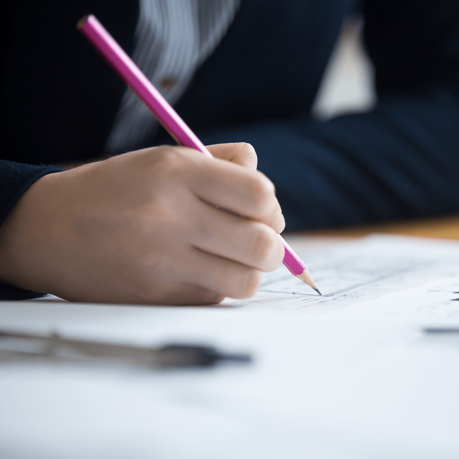 Person holding a pink pencil, writing or drawing on a sheet of paper—perhaps outlining details of an economic incentive package—with a blurred pen in the foreground.